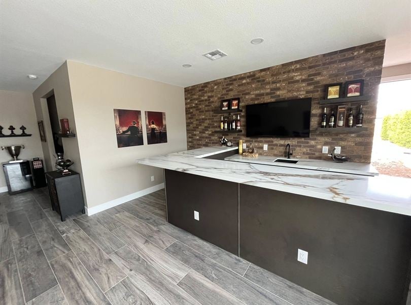 Pool house bar area with brick accent wall, stone countertop, and built-in sink
